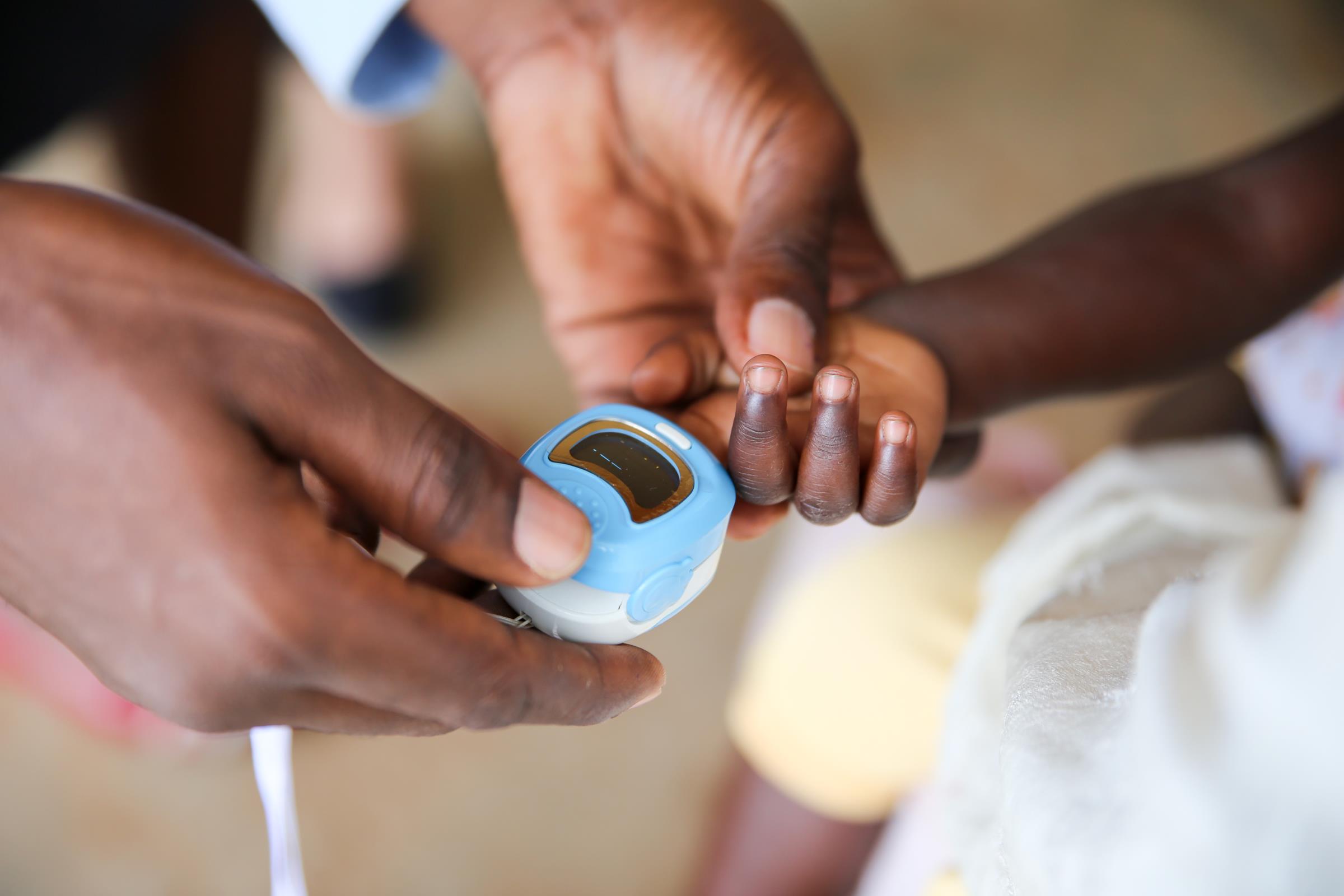 A health worker places a pulse oximeter on a child's finger.