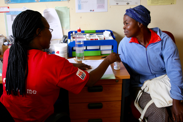 A health worker in a red shirt discusses options for HIV medication with a woman sitting across the desk from her.