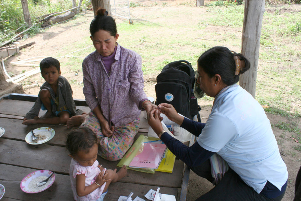 A volunteer malaria worker tests a forest worker's family for malaria at their home.