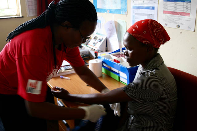 A health worker leans over a client, whose arm is outreached, as she prepares the client for HIV testing.