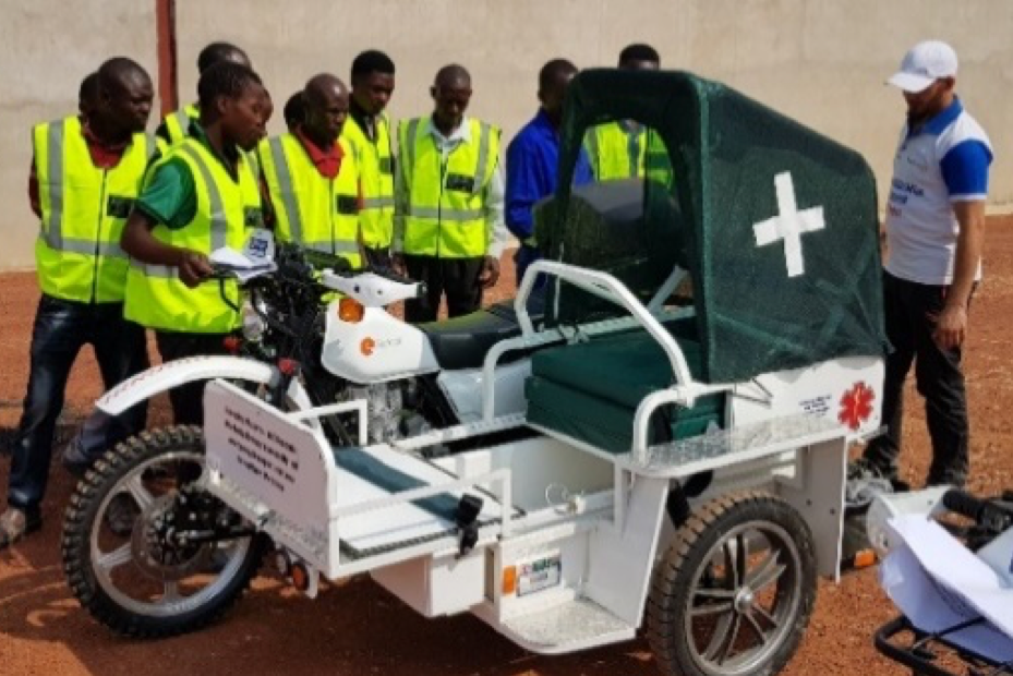 Volunteers in neon yellow vests gather around a motorcycle ambulance with a covered sidecar.