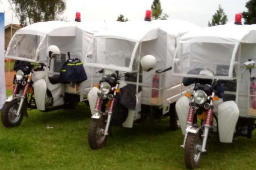 Three motorcycle ambulances lined up with helmets and vests on the handlebars, include large white covered trailers.