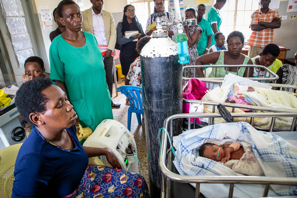 A mother sits beside her infant's hospital bed while oxygen is administered to the child.