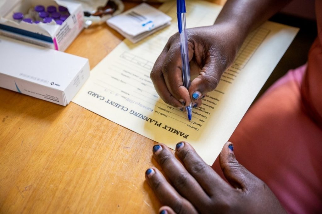 A close up of a woman's hands filling out a form on a desk. Her fingernails are painted blue.