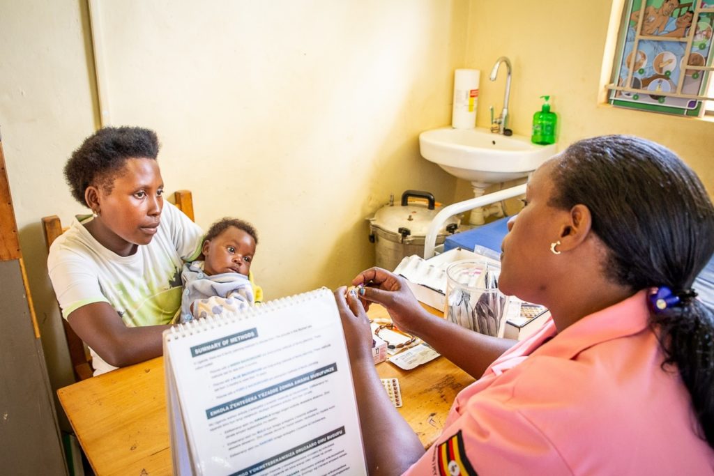 A nurse sits across a desk from a mother, who holds an infant in her arms.