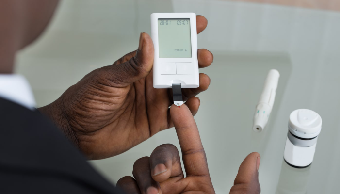 A man pricks his finger with a glucose self monitoring device, a small rectangular device with a display window to show readings of an individual's blood glucose level.