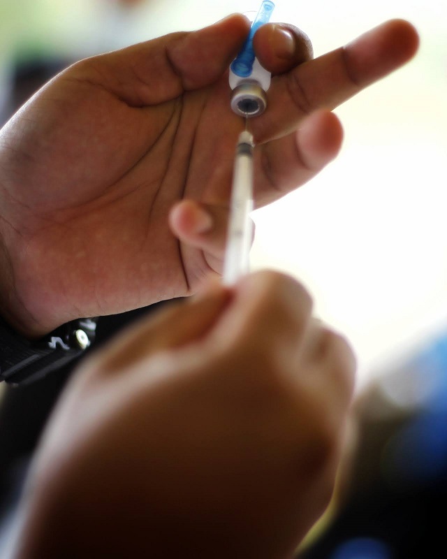 Photo shows health workers drawing vaccine from vial using a syringe